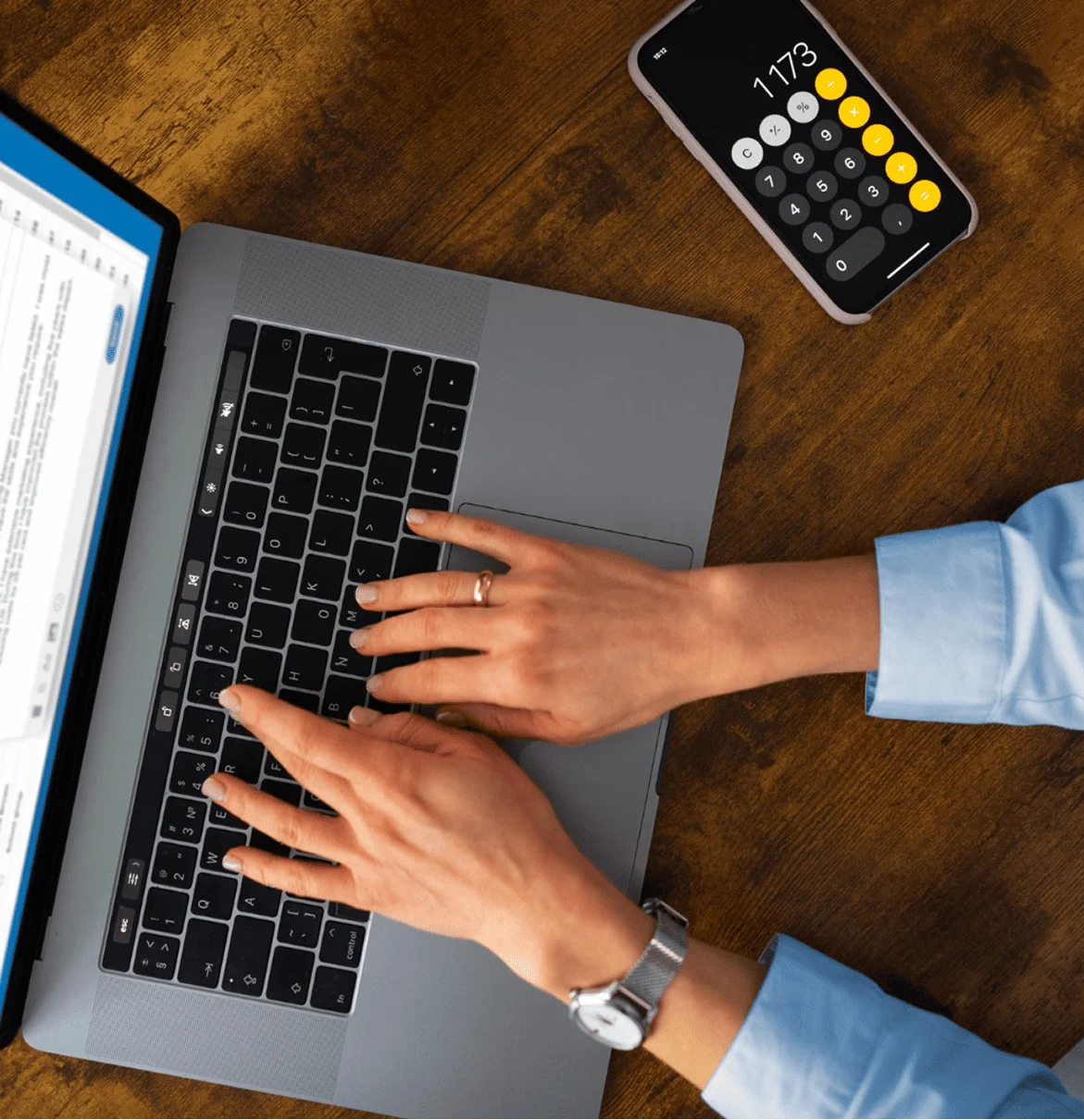 Personne en train d'écrire sur son ordinateur portable avec une calculatrice sur son téléphone à côté de lui